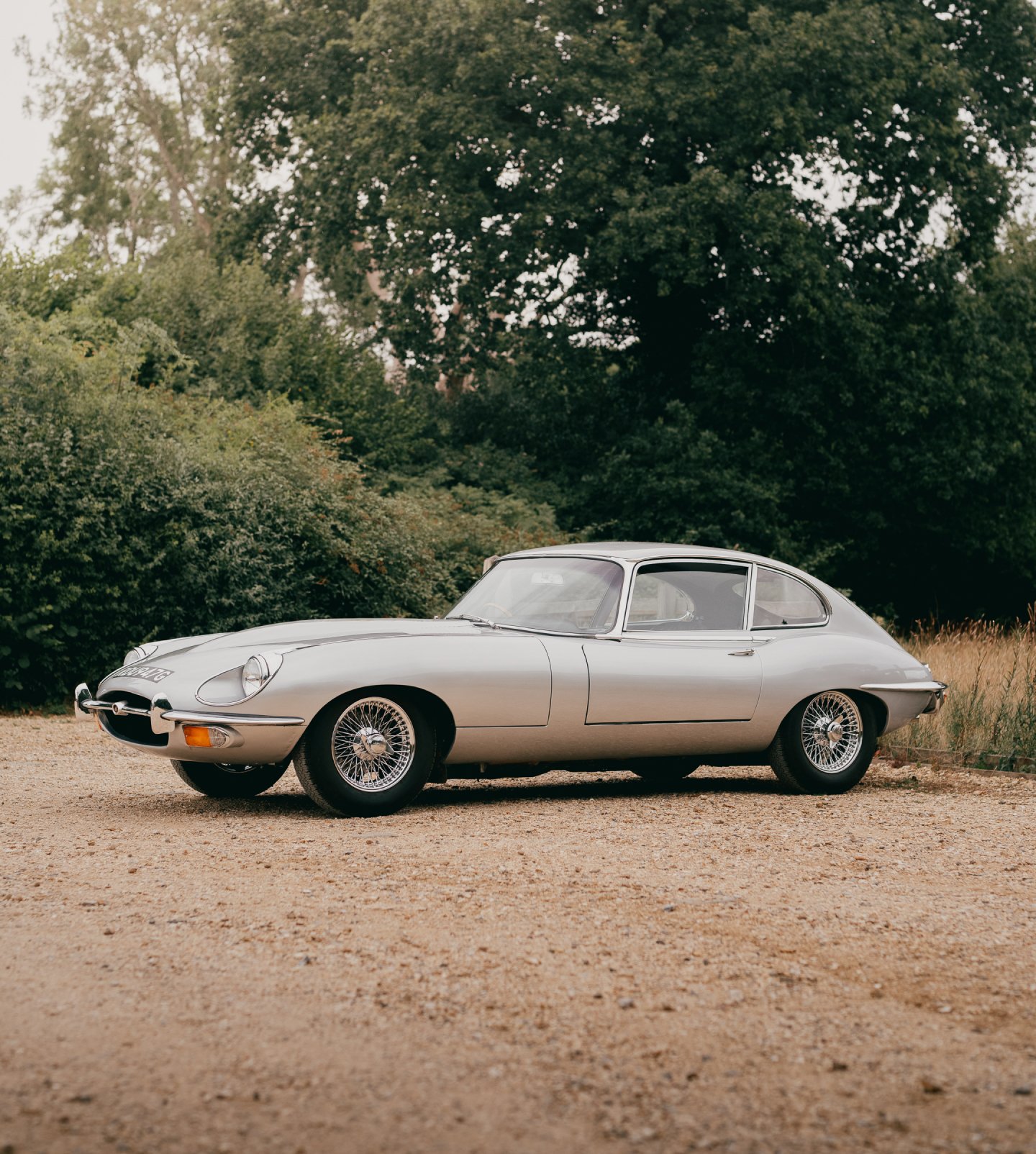 A sideview of a silver Jaguar E-type series II coupe